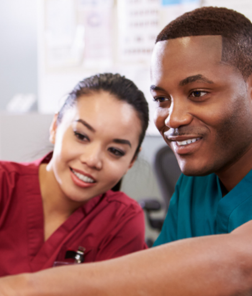 Male and female nurse in scrubs smiling while looking at computer 